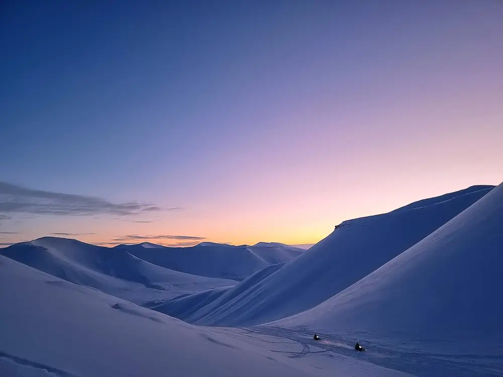 ブルーアワーの雪山を走るスノーモービル