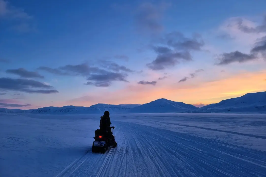 スヴァールバルのブルーアワーに雪原を走るスノーモービル