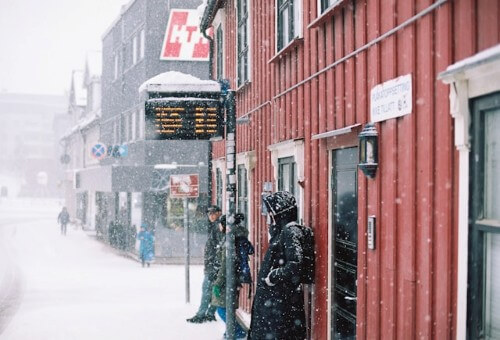 雪が降る中、バス停でバスを待つ人々