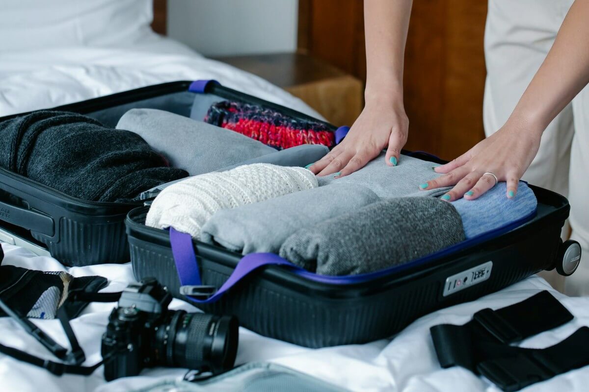 ホテルのベッドの上でスーツケースに冬服を詰めている