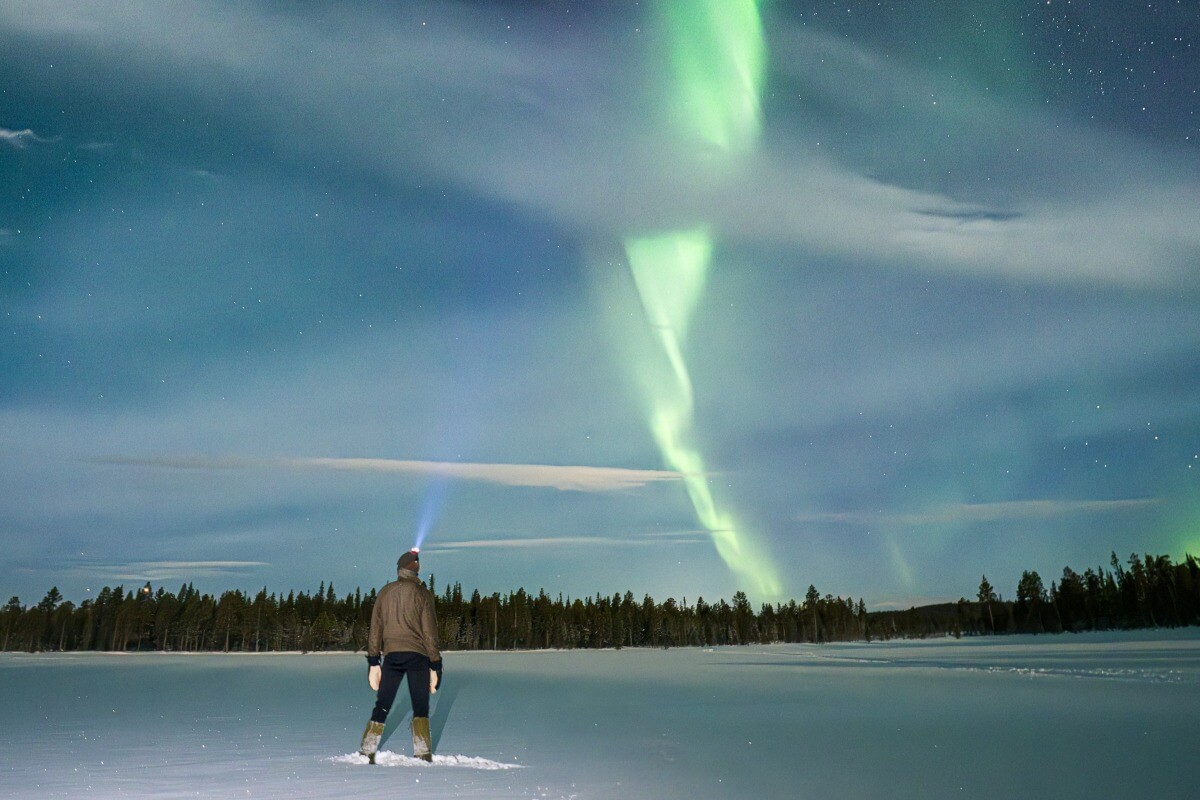 防寒対策をして、雪景色の中でオーロラを見上げる人