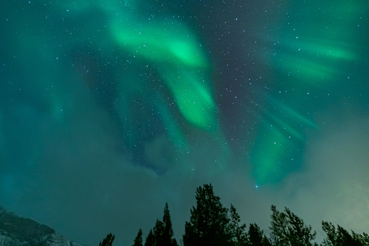 雲の合間に広がる緑のオーロラと星空（トロムソ郊外）